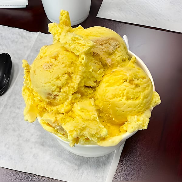 A white bowl filled with several scoops of bright yellow ice cream on a dark table.