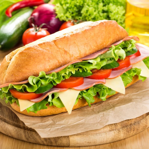 A large submarine sandwich with ham, cheese, lettuce, and tomatoes on a wooden board.